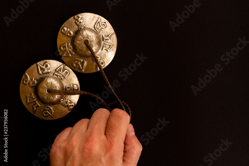 Gold karatalas Cymbals Tibetan Tingsha for meditation lies in the man's hand on a contrasting black floor. Tibetan ringing plates for relaxation and recovery during meditation. photo