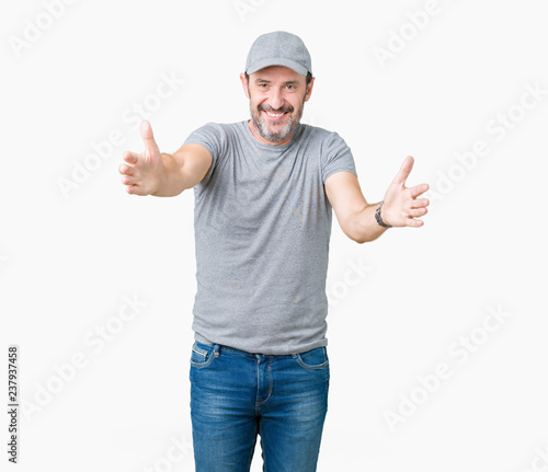 Handsome middle age hoary senior man wearing sport cap over isolated background looking at the camera smiling with open arms for hug. Cheerful expression embracing happiness.