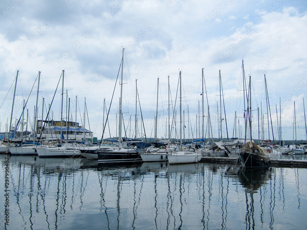 sailing yachts stand with sails lowered in a small port on a cloudy day.