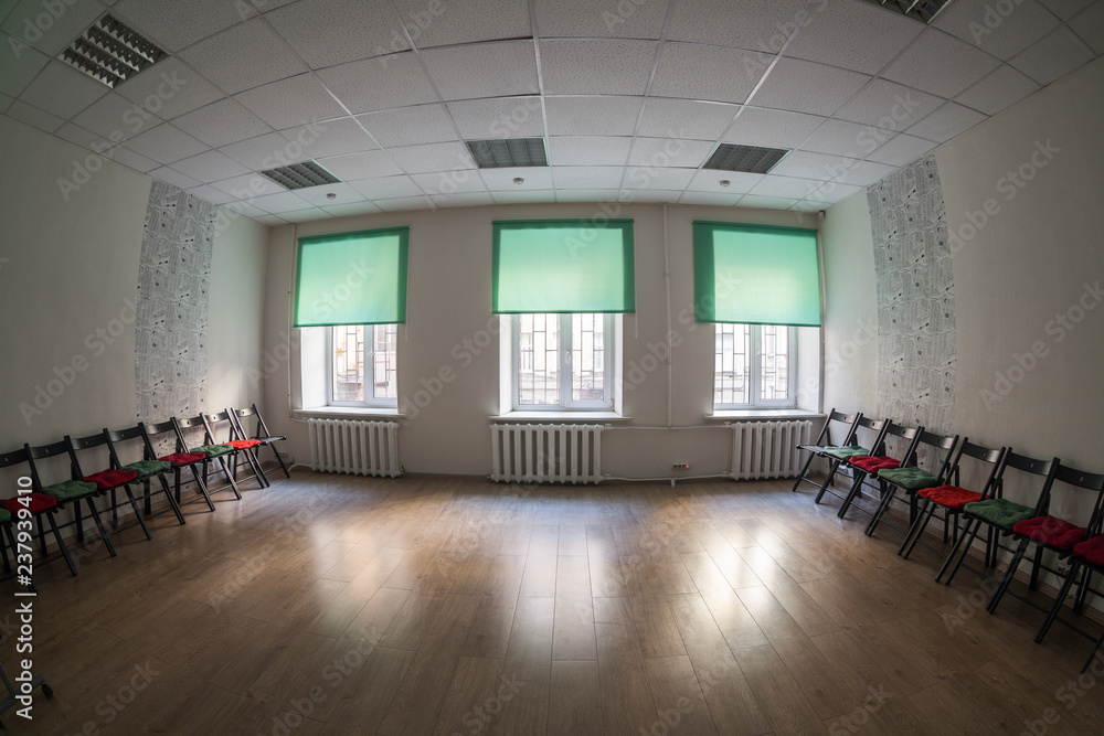 Fototapeta premium Empty dark room with three windows on wall, chairs standing on the sides and wooden hardfloor, nobody