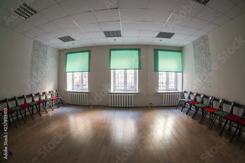 Empty dark room with three windows on wall, chairs standing on the sides and wooden hardfloor, nobody