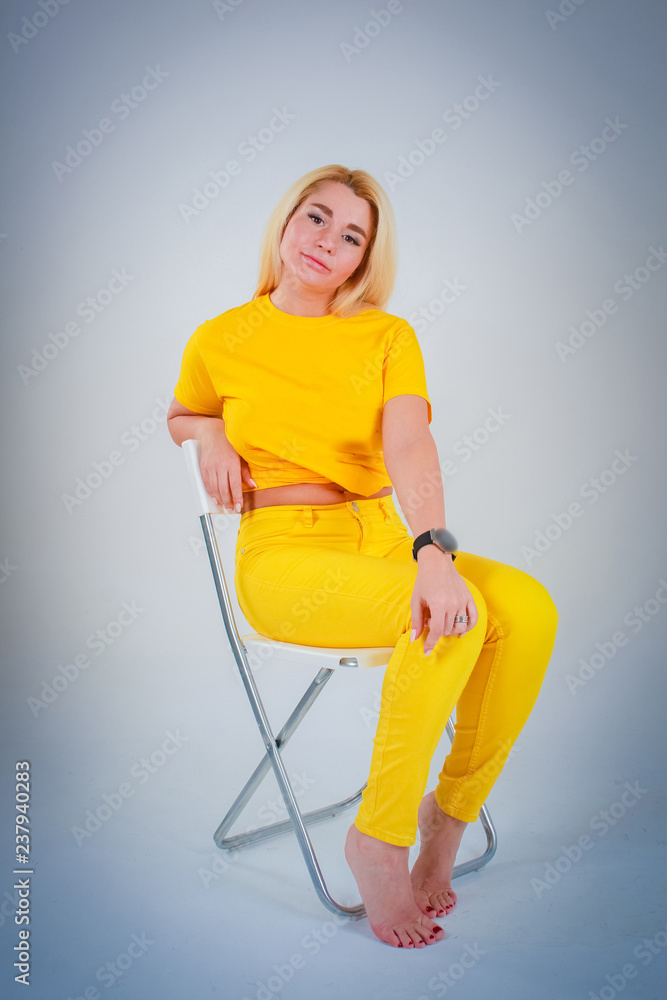 Model girl sitting on a chair with her head bent in a yellow shirt in yellow tones.
