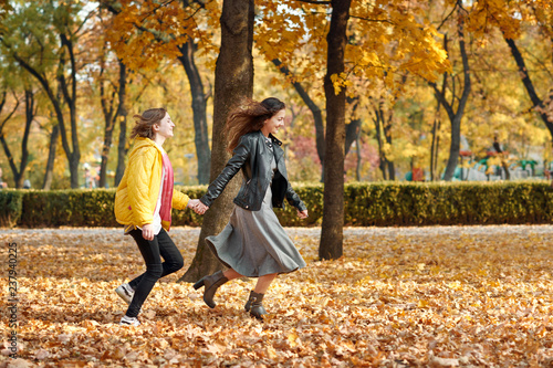 Two happy girls running in autumn city park.