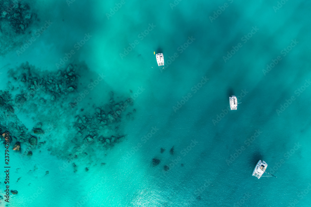 Fototapeta premium Spectacular aerial view of some yachts and small boats floating on a clear and turquoise sea, Seychelles in the Indian Ocean.Top view from drone