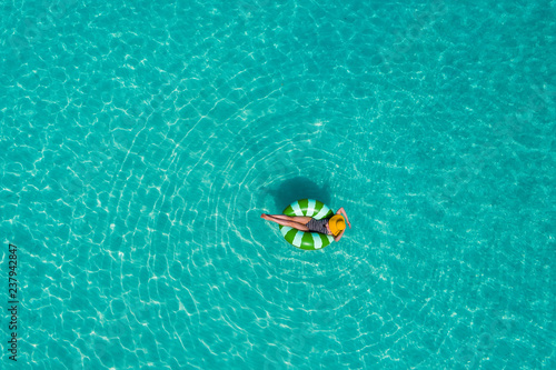 Aerial view of slim woman swimming on the swim ring donut in the transparent turquoise sea in Seychelles. Summer seascape with girl, beautiful waves, colorful water. Top view from drone