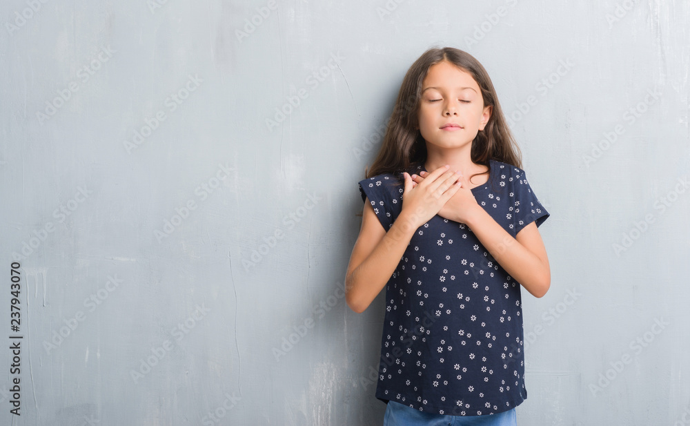 Young hispanic kid over grunge grey wall smiling with hands on chest with closed eyes and grateful gesture on face. Health concept. Young hispanic kid over grunge grey wall smiling with hands on chest with closed eyes and grateful gesture on face. Health concept.