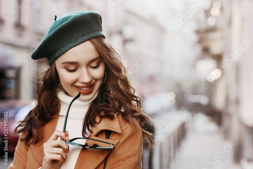 Outdoor close up portrait of young beautiful happy smiling woman with long hair wearing trendy autumn clothes, green beret,  model walking in street of european city. Copy, empty space for text