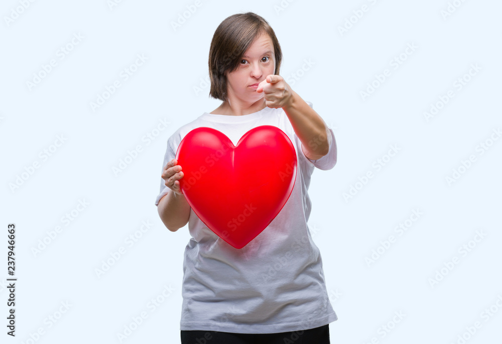 Young adult woman with down syndrome holding red heart over isolated background pointing with finger to the camera and to you, hand sign, positive and confident gesture from the front Young adult woman with down syndrome holding red heart over isolated background pointing with finger to the camera and to you, hand sign, positive and confident gesture from the front