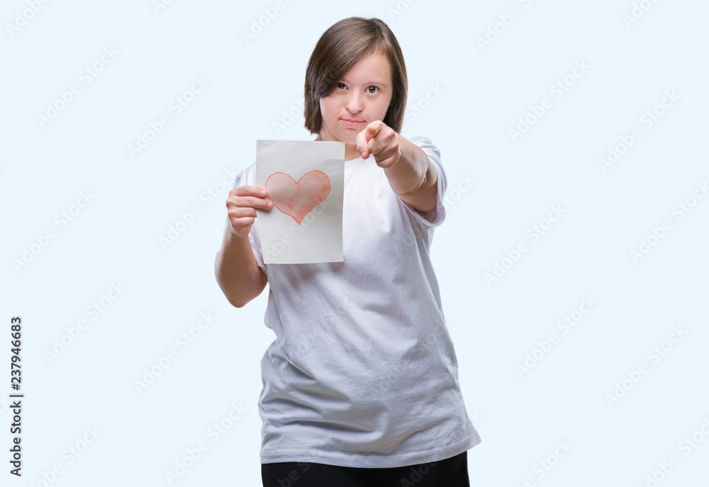 Young adult woman with down syndrome holding red heart card over isolated background pointing with finger to the camera and to you, hand sign, positive and confident gesture from the front Young adult woman with down syndrome holding red heart card over isolated background pointing with finger to the camera and to you, hand sign, positive and confident gesture from the front