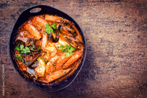 Traditional Catalan fish stew romesco de peix with prawns, mussels and fish as top view in a modern design cast-iron roasting dish with copy space right
