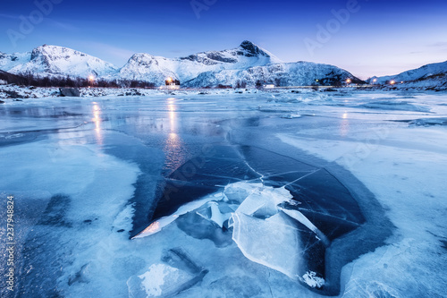 Fototapeta Naklejka Na Ścianę i Meble -  Mountain ridge and ice on the frozen lake surface. Natural landscape on the Lofoten islands, Norway. Water and mountains during sunset.