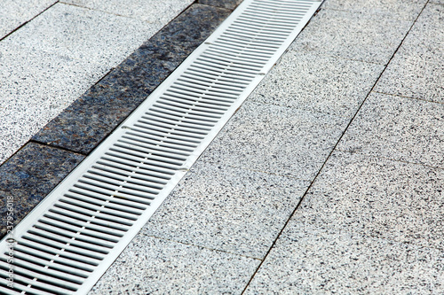 pedestrian pavement paved with stone tiles with metal drainage lattice.