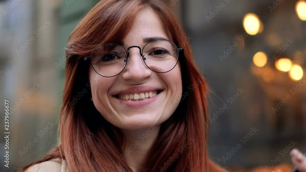 Close up portrait of attractive smiling caucasian ethnicity young ginger woman wearing eyeglasses in urban environment. Girl smiling and looking at camera in city, confident pretty. Close up portrait of attractive smiling caucasian ethnicity young ginger woman wearing eyeglasses in urban environment. Girl smiling and looking at camera in city, confident pretty.