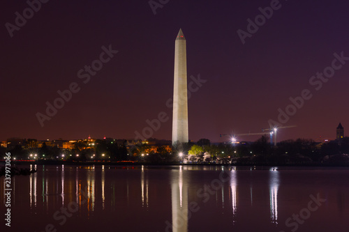 City skyline and Washington Monument at night during cherry blossom festival in Washington DC, USA. Colorful reflections of the monument and urban buildings in the water.