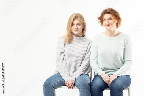 Modern adult woman with teenage girl sitting on chairs on white background. Family concept