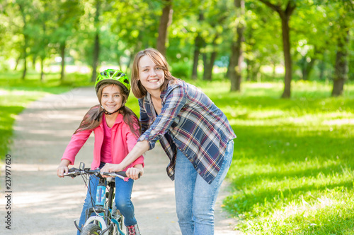 Happy young mom teaches her daughter to ride a bicycle in the park. Empty space for text