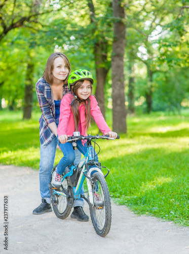 Happy family. Mother teaches her daughter to ride a bicycle in the park