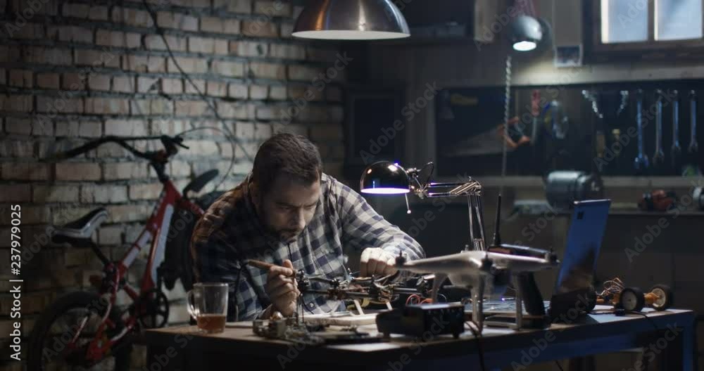 Medium shot of a man repairing and testing a drone in a garage Medium shot of a man repairing and testing a drone in a garage
