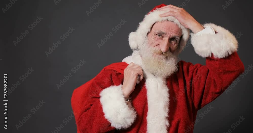 Old, kind santa with long white beard showing red bag full of chistmas gifts, isolated shoot in gray background Old, kind santa with long white beard showing red bag full of chistmas gifts, isolated shoot in gray background