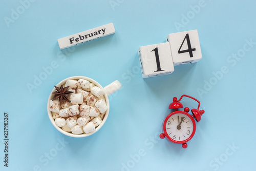 Winter composition. White wooden calendar cubes. Data February 14th. Cup of cocoa with marshmallow and red alarm clock on blue background Top view Flat lay. Concept good morning to valentines day photo