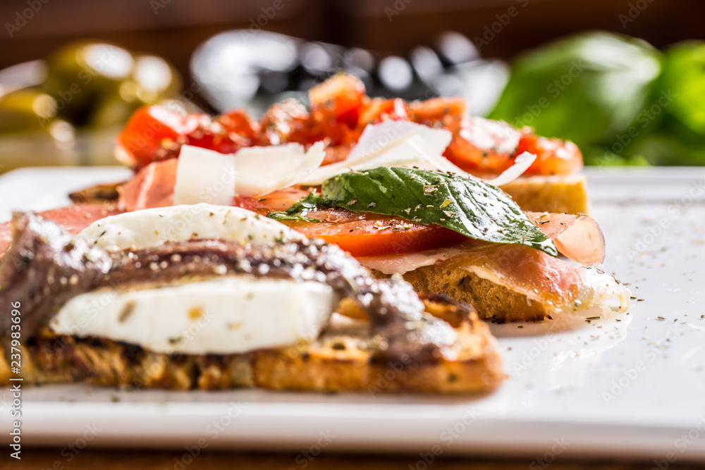 Tasty italian appetizer bruschettes with tomatoes anchovies prosciutto and mozarella Tasty italian appetizer bruschettes with tomatoes anchovies prosciutto and mozarella