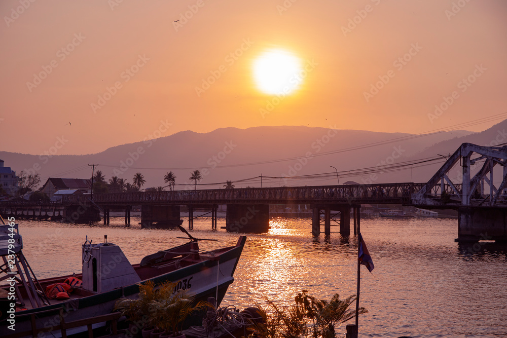 Sunset landscape with still river and distant mountains. Romantic sunset in tropical country. Urban bridge and bay