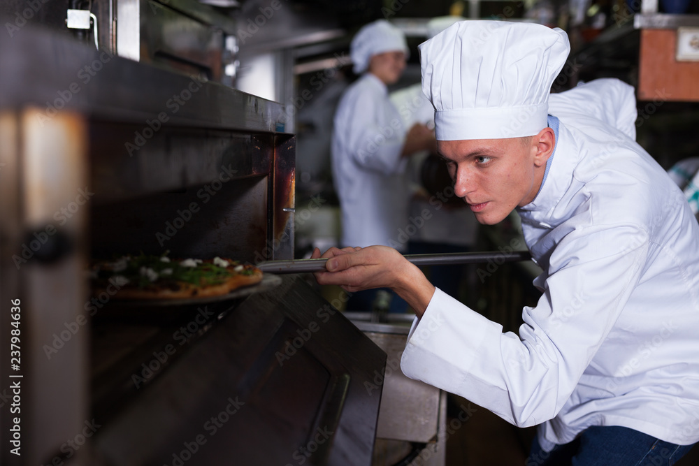 Young chef getting pizza out of oven