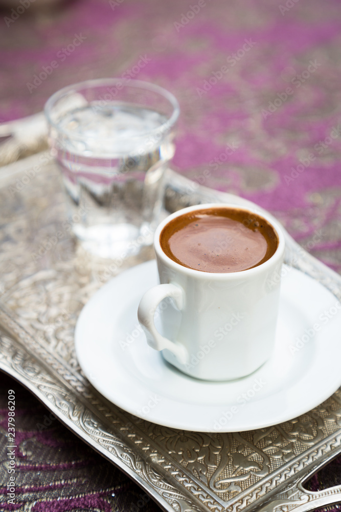 Turkish strong aromatic coffee in white porcelain cup and saucer, silver tray with glass of water on lilac table cloth, copy space, hot traditional drink, Istanbul, Turkey, Istiklal street, copy space Turkish strong aromatic coffee in white porcelain cup and saucer, silver tray with glass of water on lilac table cloth, copy space, hot traditional drink, Istanbul, Turkey, Istiklal street, copy space