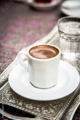 Turkish strong aromatic coffee in white porcelain cup and saucer, silver tray with glass of water on lilac table cloth, copy space, hot traditional drink, Istanbul, Turkey, Istiklal street, copy space