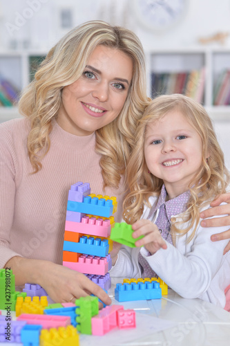Little girl and mother playing with colorful plastic blocks at h
