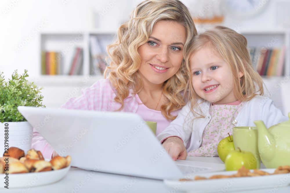 Cute young woman with girl using laptop at home