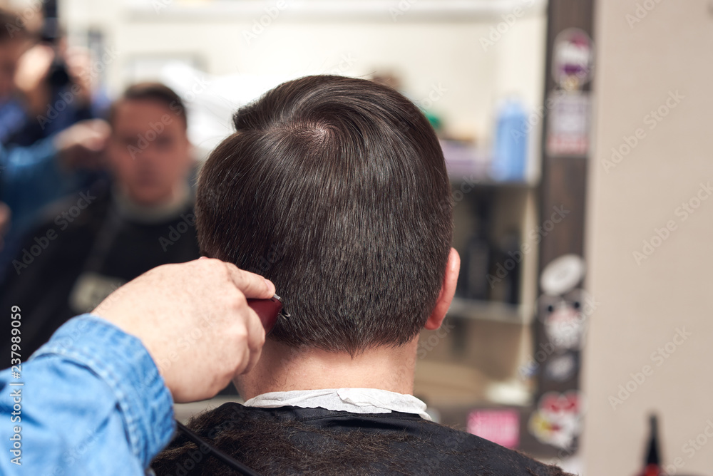 Barber making a haircut to a man with cutting machine. Back view. Barber making a haircut to a man with cutting machine. Back view.