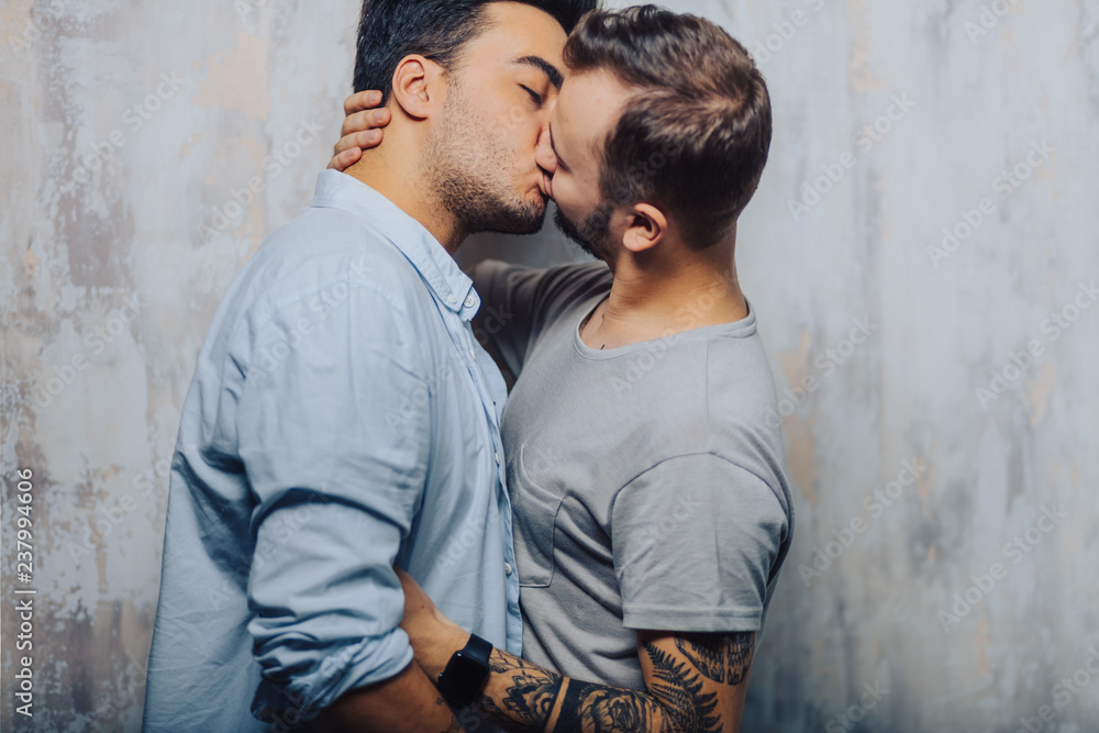 Mixed race couple of Gay Male Sexual Interactions, Asian and Caucasian men cuddling and kissing each other against grey loft background