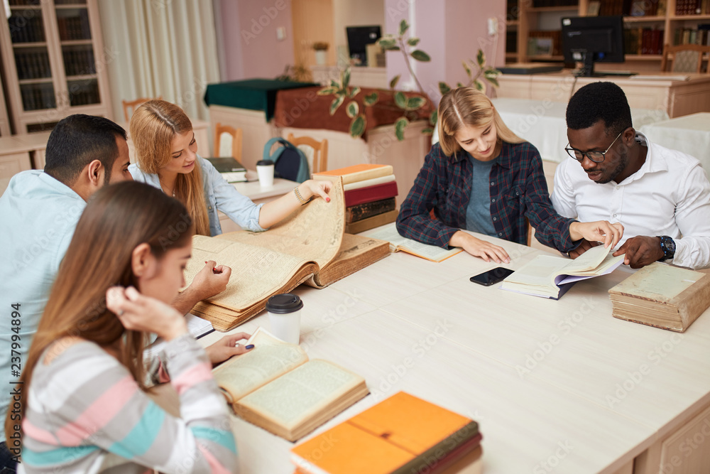 Fototapeta premium Diverse multiethnic young business partners working on new project, making investigations in old history books. Occupation, Library, Books, International Friend Concept