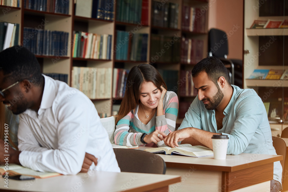 Group of concentrated multiracial diverse students reading books, drinking coffee and preparing to exam in library. People, knowledge, education and professional orientation concept Group of concentrated multiracial diverse students reading books, drinking coffee and preparing to exam in library. People, knowledge, education and professional orientation concept
