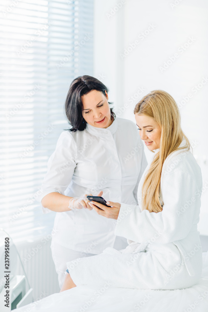 Beautiful blonde female in white bathrobe making appointment at beautician, checking vacant time at her shedule in smartphone Beautiful blonde female in white bathrobe making appointment at beautician, checking vacant time at her shedule in smartphone