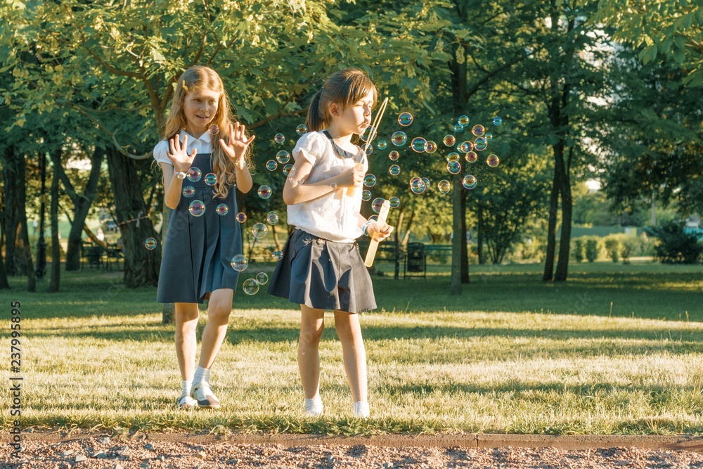 Obraz premium Two little girl friends schoolgirl 7, 8 years old play with soap bubbles on the meadow in the park.