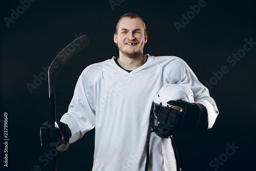 Portrait of cheerful handsome hockey player getting into the mood for winning before game starts. Sportsman in white uniform smiling at camera isolated on black