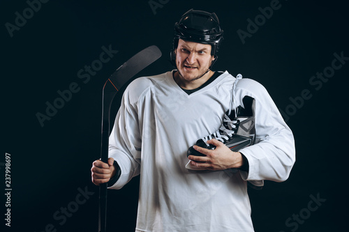 Smiling hockey player looking at camera with skates over shoulder. Isolated on blue