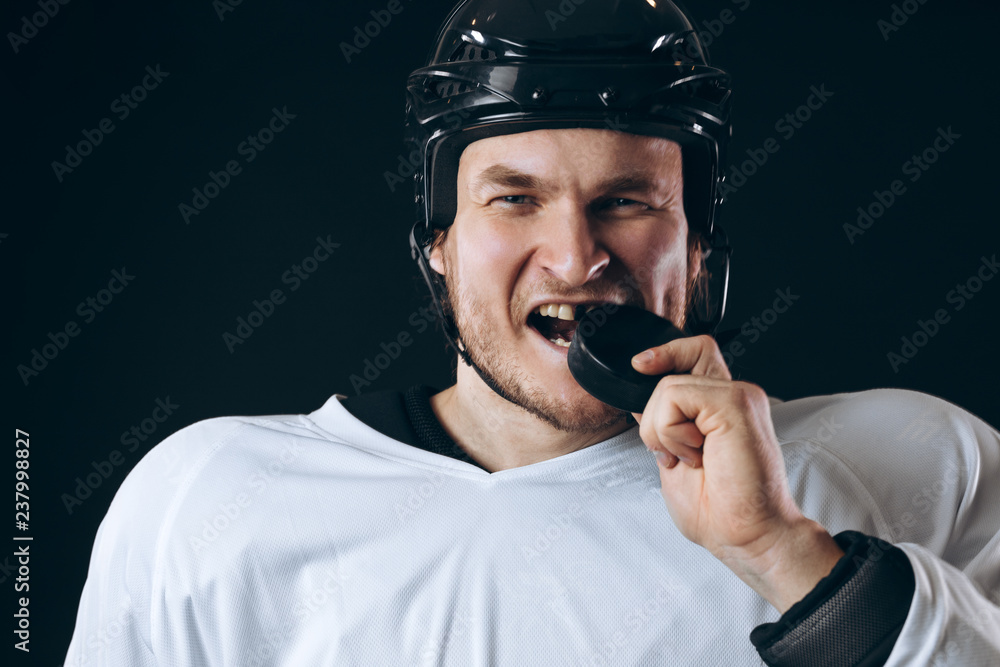 Obraz premium Caucasian Hockey player tastes the puck, having fun, demonstrates the way he lost the tooth, looking at camera isolated on black background.