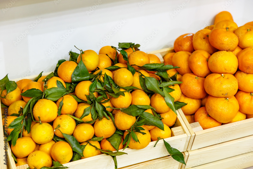 Tangerines with leaves and twigs are in a wooden box in the store on the shelf.