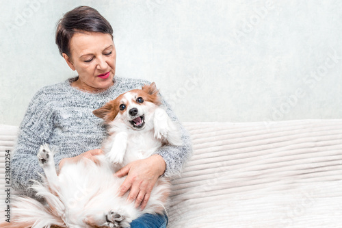 Portrait of senior woman play with her dog on sofa