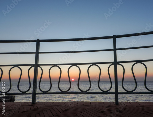 Sunset on the blue sea through iron fence of promenade, Italy