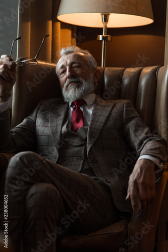 All the great events in my life occured in my later years, says elderly bearded old businessman in expensive suit clothes holding spectacles while relaxing on comfortable couch photo