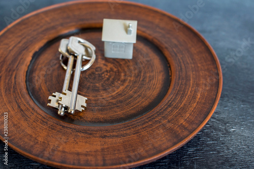 A bunch of keys lie on a vintage plate, along with an imitation of the house in the form of a metal layout.