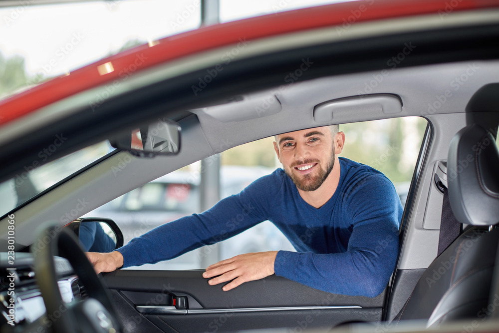 Attractive driver in blue sweater leaning on red vehicle.