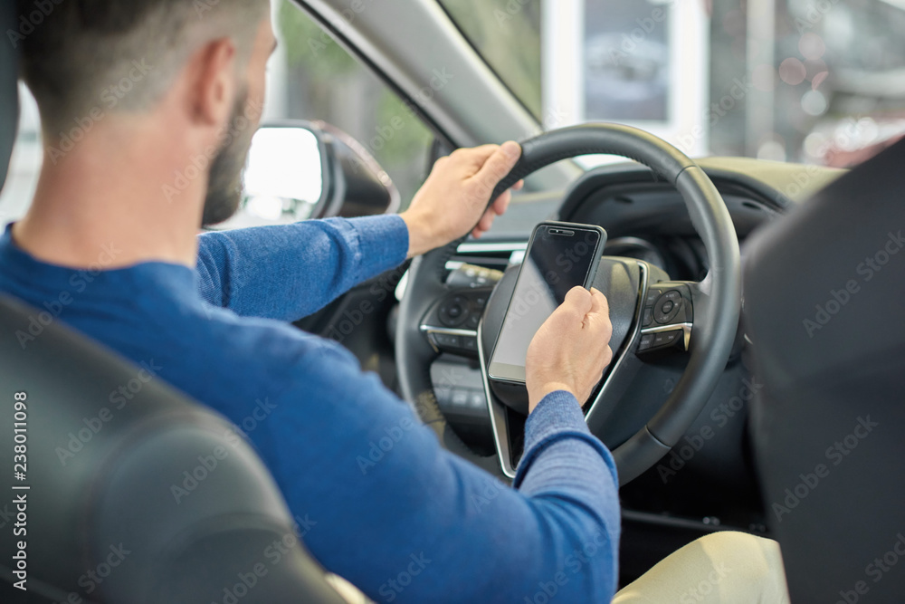 Crop of man sitting in front seat and using smartphone. Crop of man sitting in front seat and using smartphone.