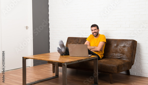 Man with his laptop in a room keeping the arms crossed while smiling