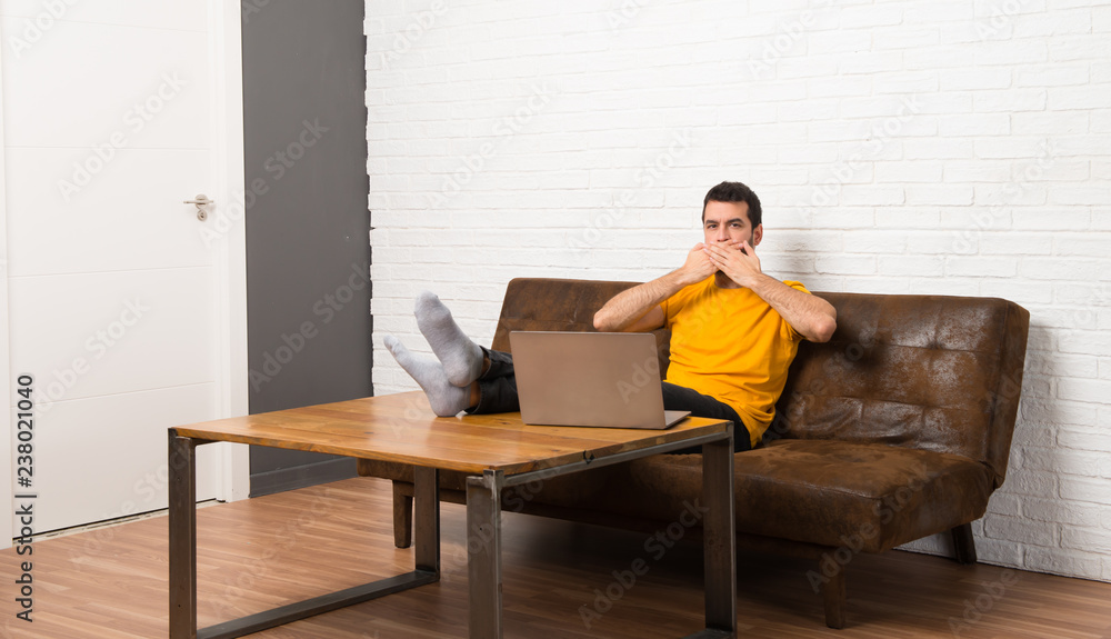 Man with his laptop in a room covering mouth with hands for saying something inappropriate