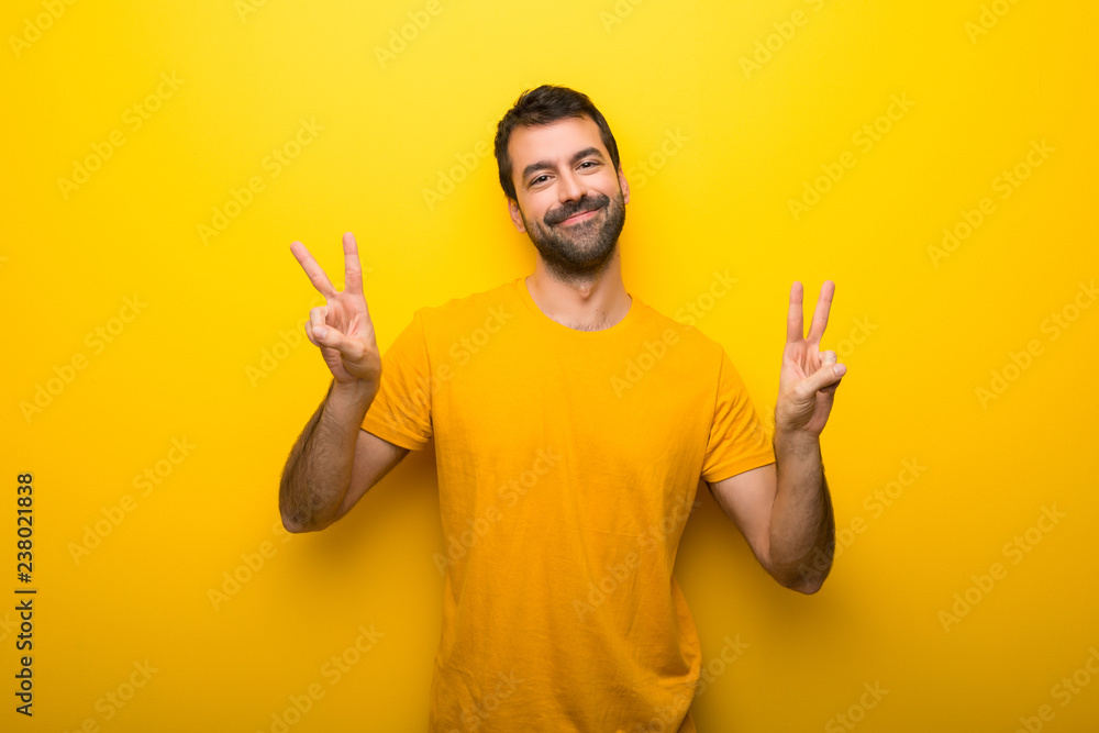 Man on isolated vibrant yellow color smiling and showing victory sign with both hands Man on isolated vibrant yellow color smiling and showing victory sign with both hands